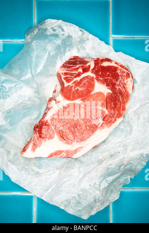 Rohes Steak auf Wachspapier auf blauer Kachel Stockfoto