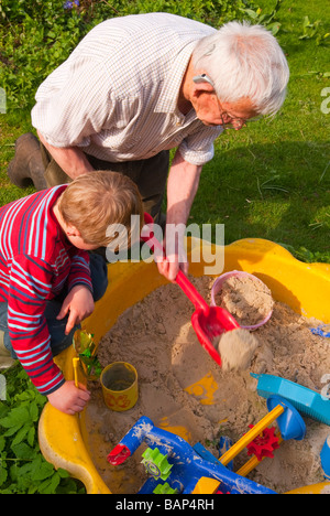 Ein Opa und sein Enkel spielen in einem Sandkasten in einem uk-Garten Stockfoto