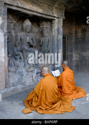 Buddhistische Mönche in orangefarbenen Gewändern vor Felsen Buddha Frescoe sitzt in Ajanta Höhlen beten Stockfoto