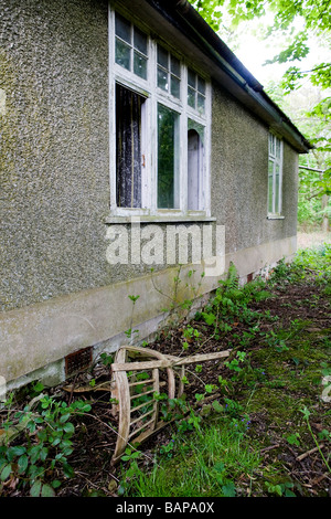 Eine verlassene Hütte liegt in einem schlechten Zustand des Landes mit Pflanzen wachsen durch die Risse und ein Alter Stuhl geworfen Stockfoto