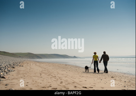 Ein junges Paar hand in hand gehen mit ihrem Hund an Newgale Strand Pembrokeshire Coast National Park Wales Sommernachmittag Stockfoto