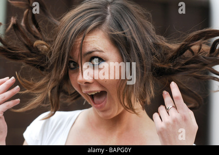 Attraktive Brünette junge Frau trägt Balmain Haarverlängerungen flicking Haar im wind Stockfoto