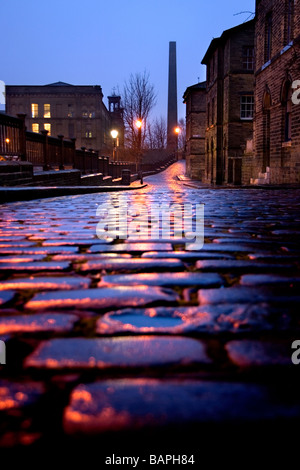 Ein Blick auf die gepflasterte Straße von Albert Terrace, mit Blick von Salts Mill und einem Kamin, Saltaire, Bradford, West Yorkshire Stockfoto