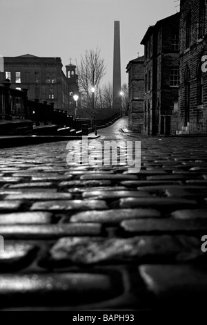 Ein Blick auf die gepflasterte Straße von Albert Terrace, mit Blick von Salts Mill und einem Kamin, Saltaire, Bradford, West Yorkshire Stockfoto