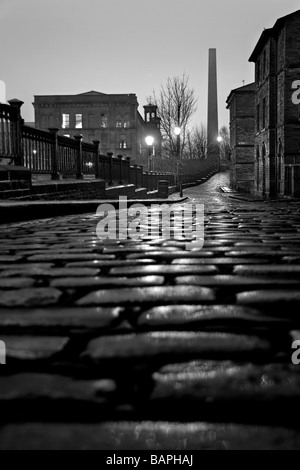 Ein Blick auf die gepflasterte Straße von Albert Terrace, mit Blick von Salts Mill und einem Kamin, Saltaire, Bradford, West Yorkshire Stockfoto