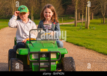 Ein Junge und ein Mädchen spielen auf eine batteriebetriebene Fahrt auf Spielzeug Jeep fahren auf eine private Fahrt auf dem Land Stockfoto