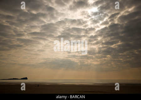 Die Sonne bricht durch die Wolken über einem Strand. Stockfoto