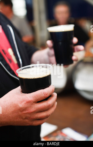 Mann, hält zwei Pints Stout in Kunststoff Pint Gläser Stockfoto