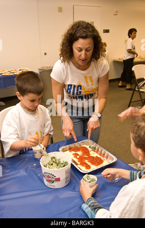 Eine Frau zeigt zwei junge Kinder wie man Lasagne an der Universität Synagoge, Big Sunday, Community Outreach. Stockfoto