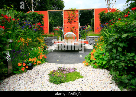 Großes Glas Kugel-Wasser-Funktion auf einem gepflasterten Kreis umringt von einer Spiegelwand und Grenzen mit Stauden bepflanzt. Stockfoto