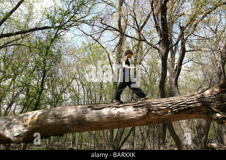 Ein 12 Jahre alter Junge, zu Fuß über einen umgestürzten Baum in einem Wald. Stockfoto