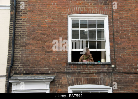 Alte Frau, die gerade einer Parade aus ihrem Fenster in Hastings, West Sussex, England, UK Stockfoto