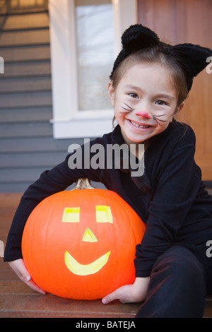 Junges Mädchen Mischlinge in Katze Kostüm Halloween-Kürbis hält Stockfoto