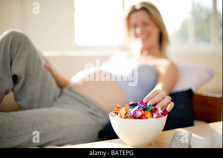 Schwangere Frau entspannen auf dem Sofa mit einer Schüssel Schokoladenbonbons. Stockfoto