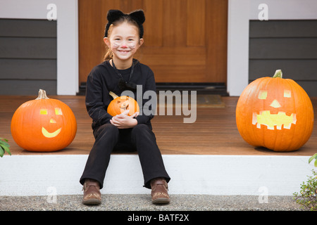 Junges Mädchen Mischlinge in Katze Kostüm Halloween-Kürbis hält Stockfoto