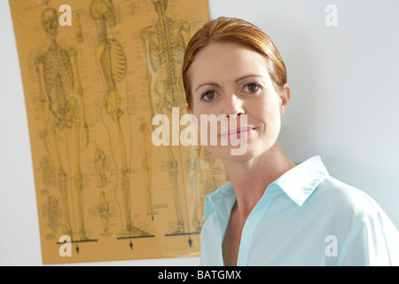 Chiropraktiker in ihrer Praxis. Hinter ihr ist ein Diagramm, einschließlich drei Diagramme des menschlichen Skeletts. Stockfoto