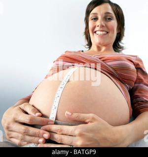 Schwangere Frau auf einem Untersuchungstisch mit einem Maßband über ihren geschwollenen Bauch. Stockfoto