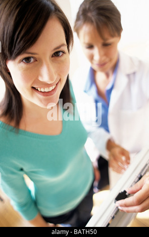 Gewichts-Check-Up. Allgemeinmedizin Arzt einstellen der Balance auf Weighingscales beim Wiegen einer junge Patientin. Stockfoto