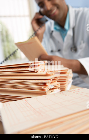 Patientenakten auf Schreibtisch des Arztes. Der Arzt ist mit Telefon und mit Blick auf eine der Platten. Stockfoto