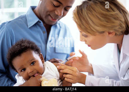 Kindheit-Injektion. Arzt einem 5 Monate alten Jungen eine Injektion geben, während er in des Vaters Schoß sitzt. Stockfoto