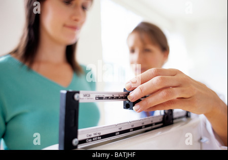 Gewichts-Check-Up. Allgemeinmedizin Arzt einstellen der Balance auf Waagen beim Wiegen einer junge Patientin. Stockfoto