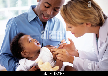 Kindheit-Injektion. Arzt einem 5 Monate alten Jungen eine Injektion geben, während er in des Vaters Schoß sitzt. Stockfoto