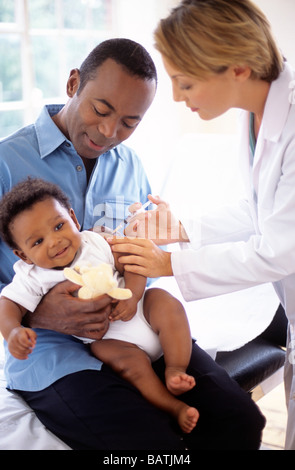 Kindheit-Injektion. Arzt einem 5 Monate alten Jungen eine Injektion geben, während er in seinem Vater Schoß sitzt. Stockfoto