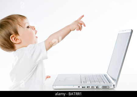 Baby Junge sitzt neben Notebook und auf etwas gerichtet Stockfoto