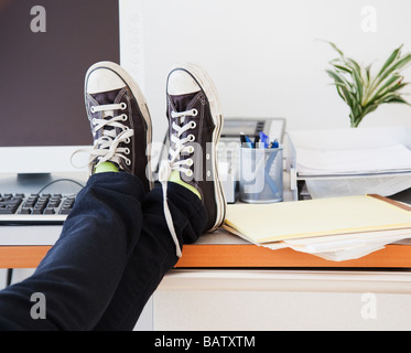 Junge Büroangestellte in Freizeitkleidung entspannend im Büro mit den Beinen am Schreibtisch Stockfoto