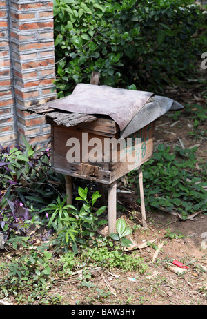 Holz Bienenstock außerhalb in der Nähe einer Wand in einem Feld-Wald auf der Erde mit Bienen fliegen herum. Es ist handgefertigt. Sonne Urlaub Sehenswürdigkeiten Stockfoto