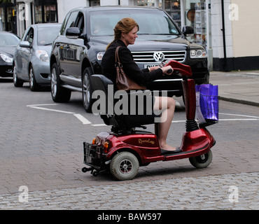 Frau sitzend auf einem Rascal Mobilität Scooter kreuzt die Straße an einem Fußgängerüberweg Stockfoto