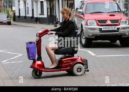 Frau sitzend auf einem Rascal Mobilität Scooter kreuzt die Straße an einem Fußgängerüberweg Stockfoto