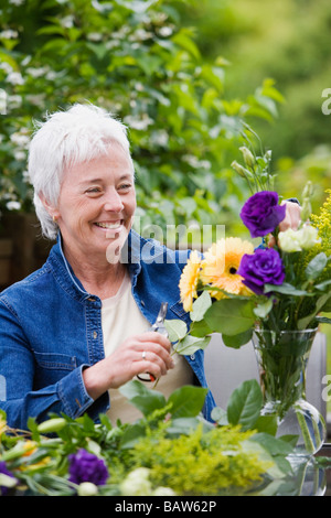 Ältere Frau lächelnd und Anordnen von Blumen in vase Stockfoto