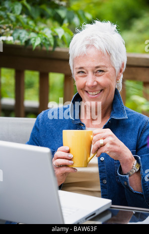 Ältere Frau mit Kaffee und Laptop im freien Stockfoto