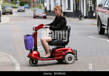 Frau sitzend auf einem Rascal Mobilität Scooter kreuzt die Straße an einem Fußgängerüberweg Stockfoto