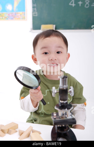 Junge sitzt am Mikroskop, Lupe lächelnd halten Stockfoto