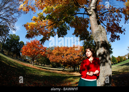 Eine hübsche junge Frau lehnt sich an einen Baum in einem Park während der Herbstsaison in Victoria, BC, Kanada. Stockfoto