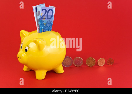 interessieren Sie Konzept - gelbe Sparschwein mit 20 Euro-Schein in Schlitz und verschiedene Münzen dahinter Stockfoto