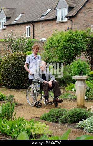 Krankenschwester schob einen männlichen Patient im Rollstuhl durch einen schönen Garten Stockfoto