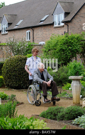 Krankenschwester schob einen männlichen Patient im Rollstuhl durch einen schönen Garten Stockfoto