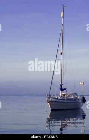 Eine einsame Yacht schwimmt eine am frühen Abend auf den stillen Wassern am Eingang zum Hafen von Weymouth in Dorset, England. Stockfoto