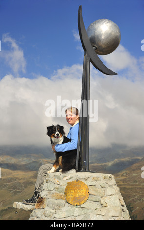 Eine junge Frau Wanderer mit ihrem Hund sitzt auf einer Skulptur des Neptun auf dem Planeten-Wanderweg in den Schweizer Alpen. Stockfoto