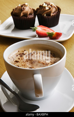 Eine Tasse Latte Kaffee und Schokolade Cupcakes mit Erdbeeren. Stockfoto