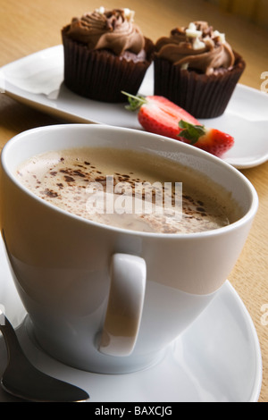 Eine Tasse Latte Kaffee und Schokolade Cupcakes mit Erdbeeren. Stockfoto