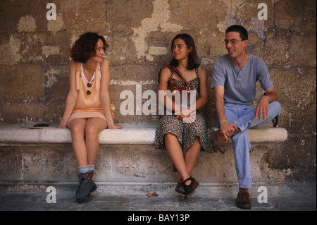 Zwei junge Frauen und ein junger Mann sitzt auf einer Steinbank im Innenhof des Colegio de Santa Cruz, Valladolid, Kastilien-Leo Stockfoto