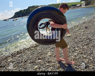 Teenager mit Gummiring, aufblasbaren Reifen, am Strand von Lulworth Cove, Südengland, Großbritannien Stockfoto