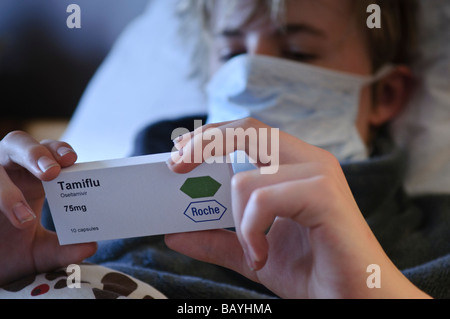 Teenager liest Rückseite Tamiflu Feld beim liegen im Bett mit einer Maske Stockfoto