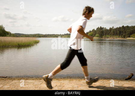 Ein Jogger läuft Paased an den Ufern des Frensham Teiche in England. Stockfoto