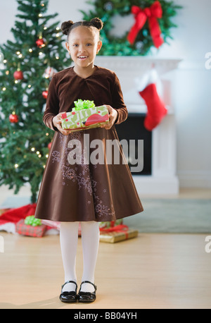 Afroamerikanische Mädchen im Kleid hält Weihnachtsgeschenk Stockfoto