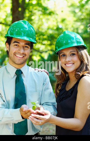 Hispanische Geschäftsleute mit grünen Arbeitshelme halten Baum keimen Stockfoto